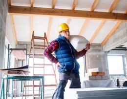 Image of a man at a work site rubbing his back as he carries a heavy sack 
