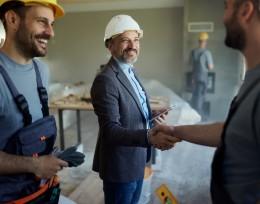 Image of 3 men at a work site in hard hats, 2 are shaking hands