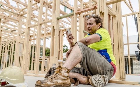 Image of a man at a work site sitting down on his mobile phone